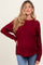 woman wearing a burgundy maternity sweater with a textured knit and relaxed fit, showcasing her baby bump