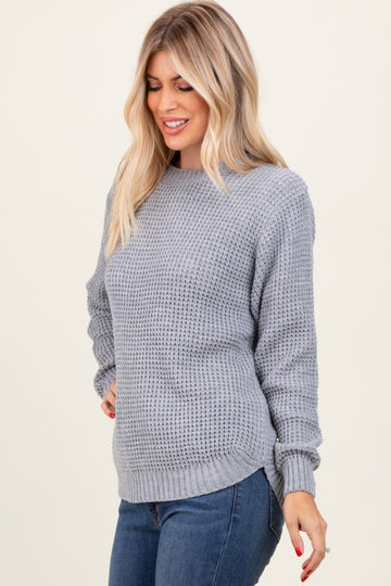 woman wearing a light grey textured knit sweater with long sleeves and side slits, paired with denim jeans