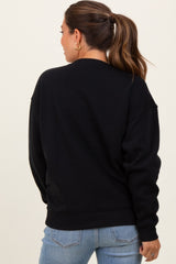 woman wearing a black oversized maternity sweatshirt, shown from the back, paired with light blue jeans