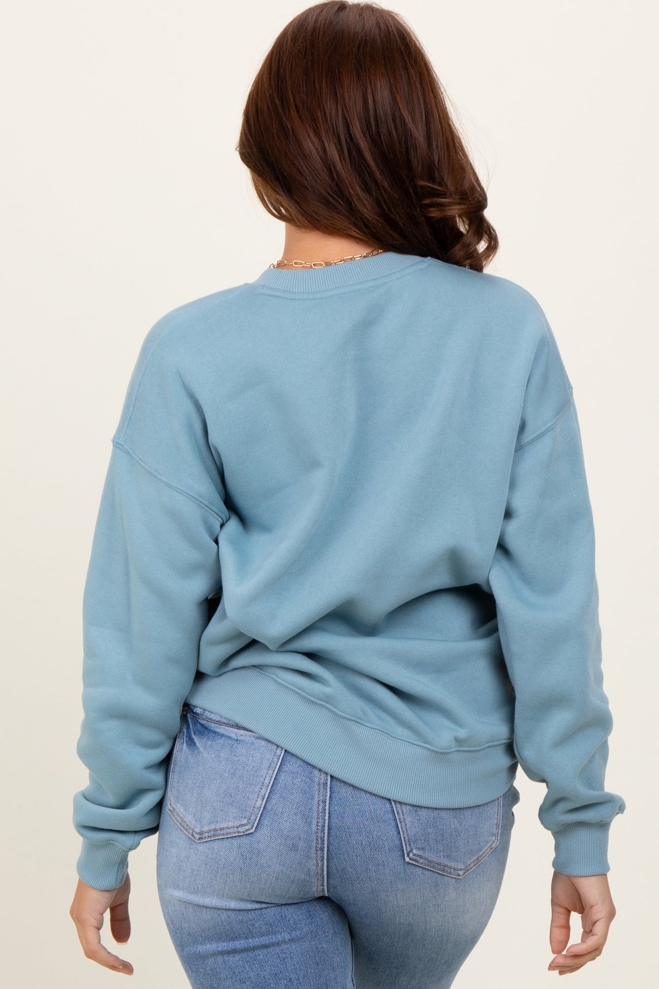 woman wearing a light blue oversized sweatshirt with a relaxed fit and ribbed cuffs, viewed from the back