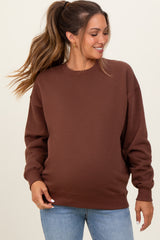 woman wearing a brown oversized maternity sweatshirt with a relaxed fit and smiling while showing her baby bump
