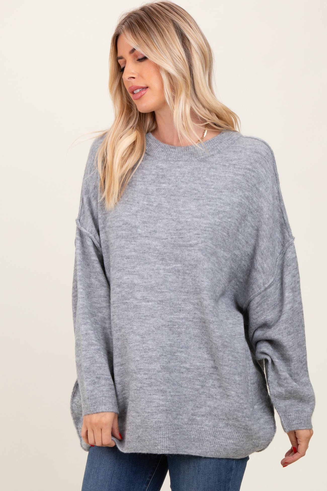 woman wearing a light gray oversized sweater with dropped shoulders and a relaxed fit, styled with blue jeans