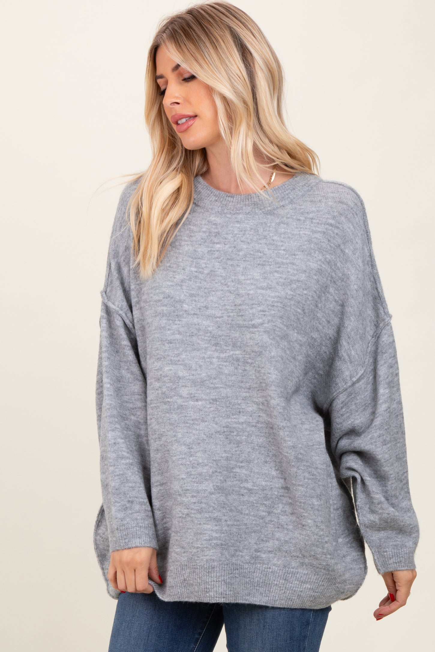woman wearing a light gray oversized sweater with dropped shoulders and a relaxed fit, styled with blue jeans