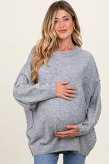 woman wearing a gray oversized maternity sweater and holding her baby bump