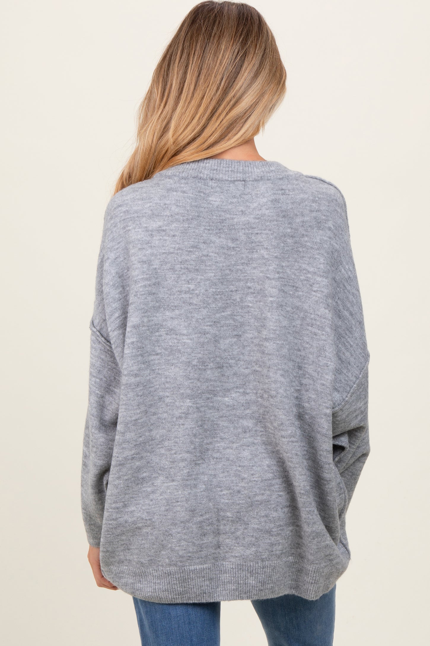 woman wearing a gray oversized maternity sweater, seen from the back, paired with blue jeans