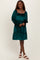woman wearing a dark green velvet smocked dress with long sleeves and a tiered hem