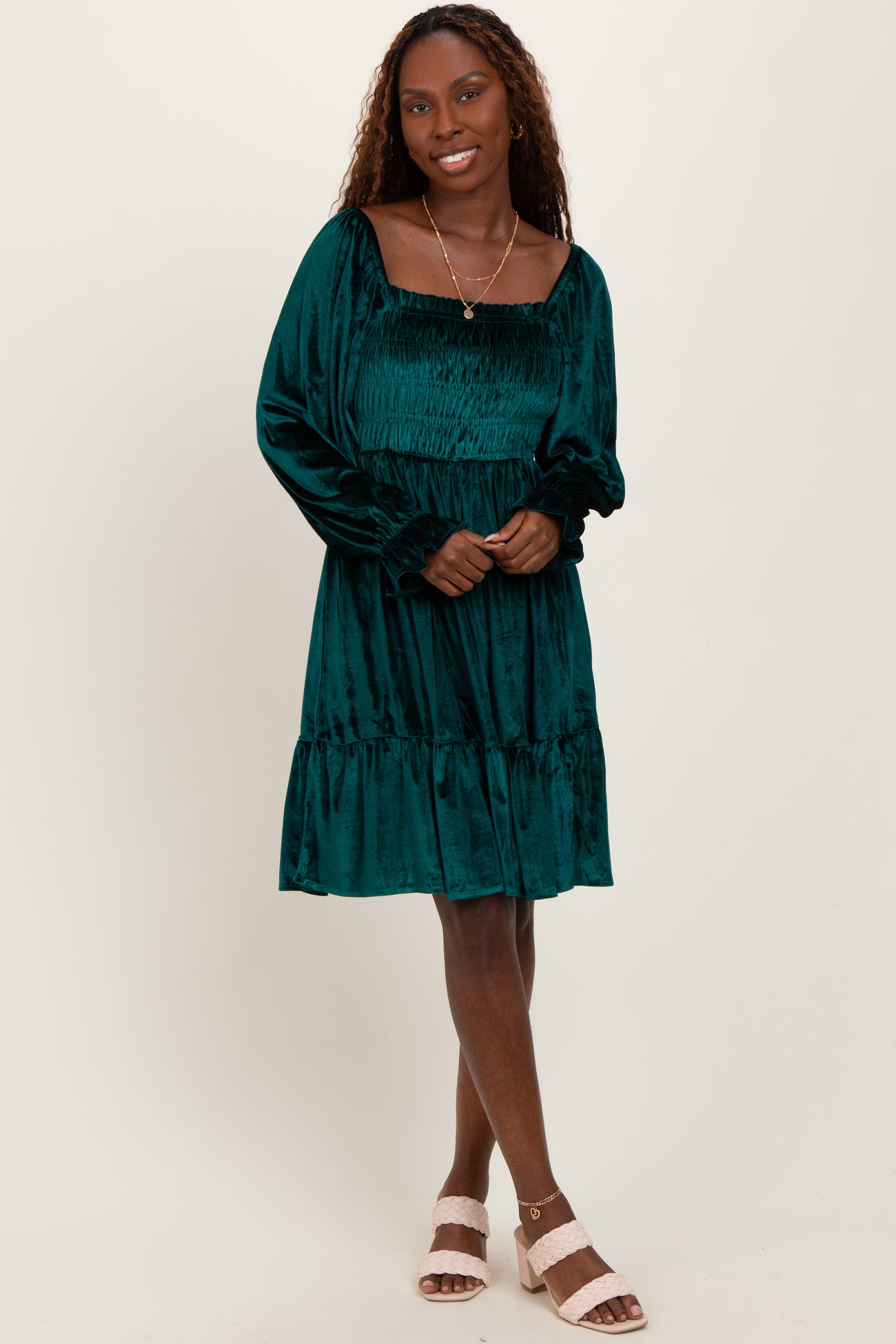 woman wearing a dark green velvet smocked dress with long sleeves and a tiered hem