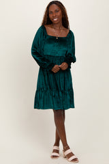 woman wearing a dark green velvet smocked dress with long sleeves and a tiered hem