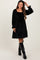 woman wearing a black velvet maternity dress with smocked bodice and puff sleeves, standing with hand in hair