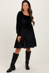 woman wearing a black velvet maternity dress with long sleeves and a tiered skirt, smiling and standing with one hand on her hip