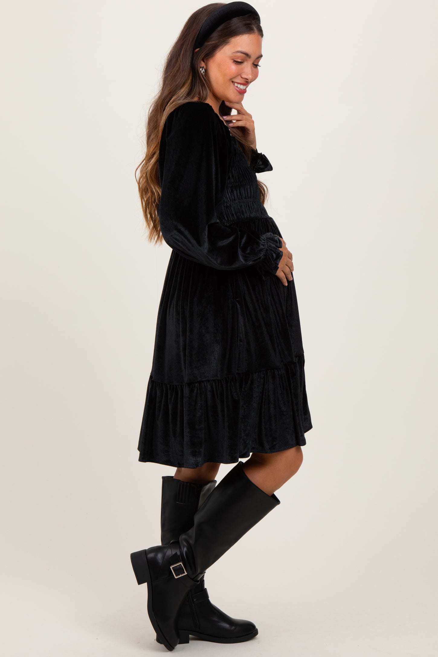 woman wearing a black velvet maternity dress with long sleeves and a tiered skirt, showing her baby bump