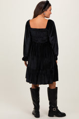 woman wearing a black velvet maternity dress with a smocked back and long sleeves, paired with knee-high black boots
