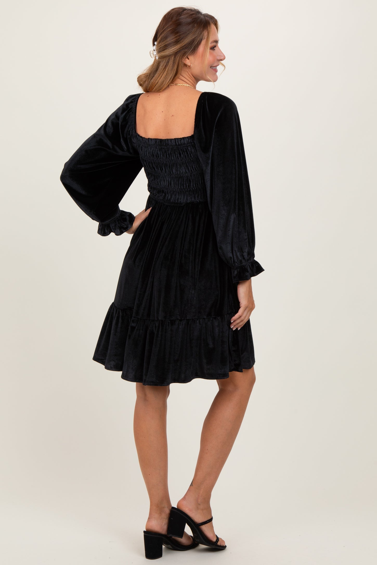 woman wearing a black velvet smocked dress with long sleeves and a tiered skirt, standing with her back to the camera