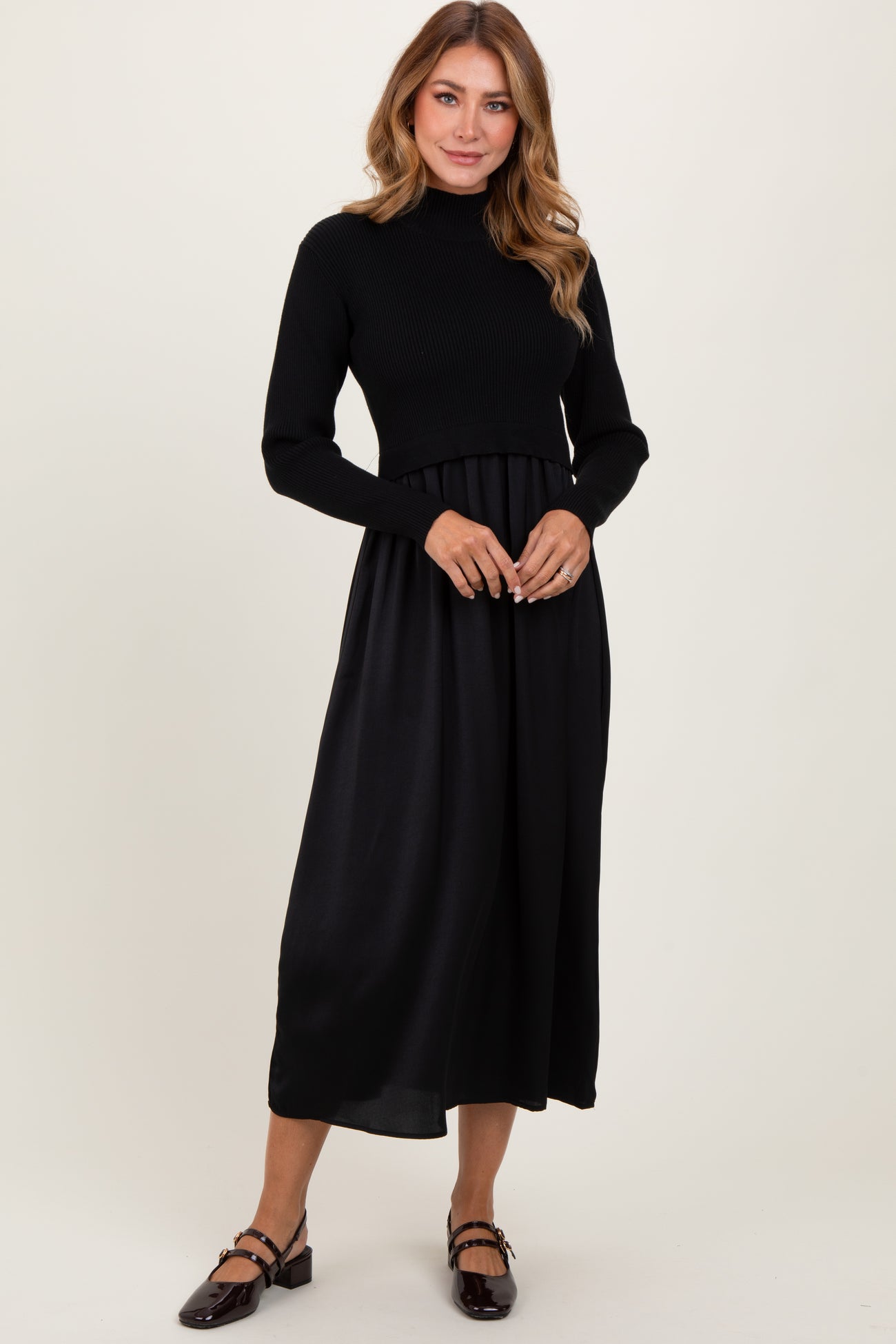 woman wearing a black knit long sleeve dress with a flowy satin skirt and flat shoes