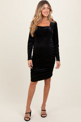 woman wearing a black long sleeve maternity dress with a square neckline and gathered details, showcasing her baby bump