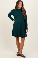 woman wearing a dark green long sleeve maternity dress with a flared skirt and a visible baby bump
