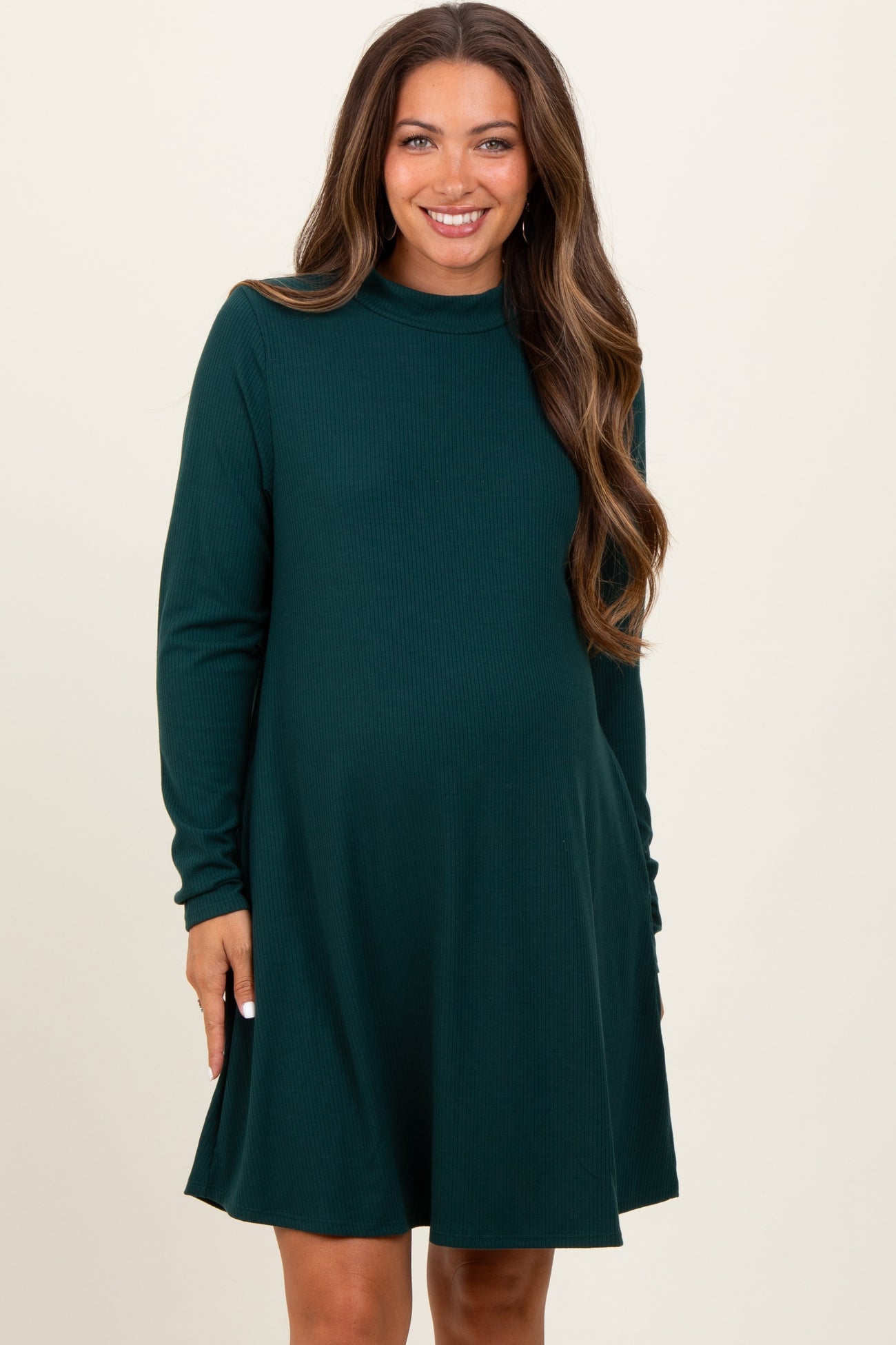 woman wearing a dark green long sleeve maternity dress with a flared skirt and visible baby bump
