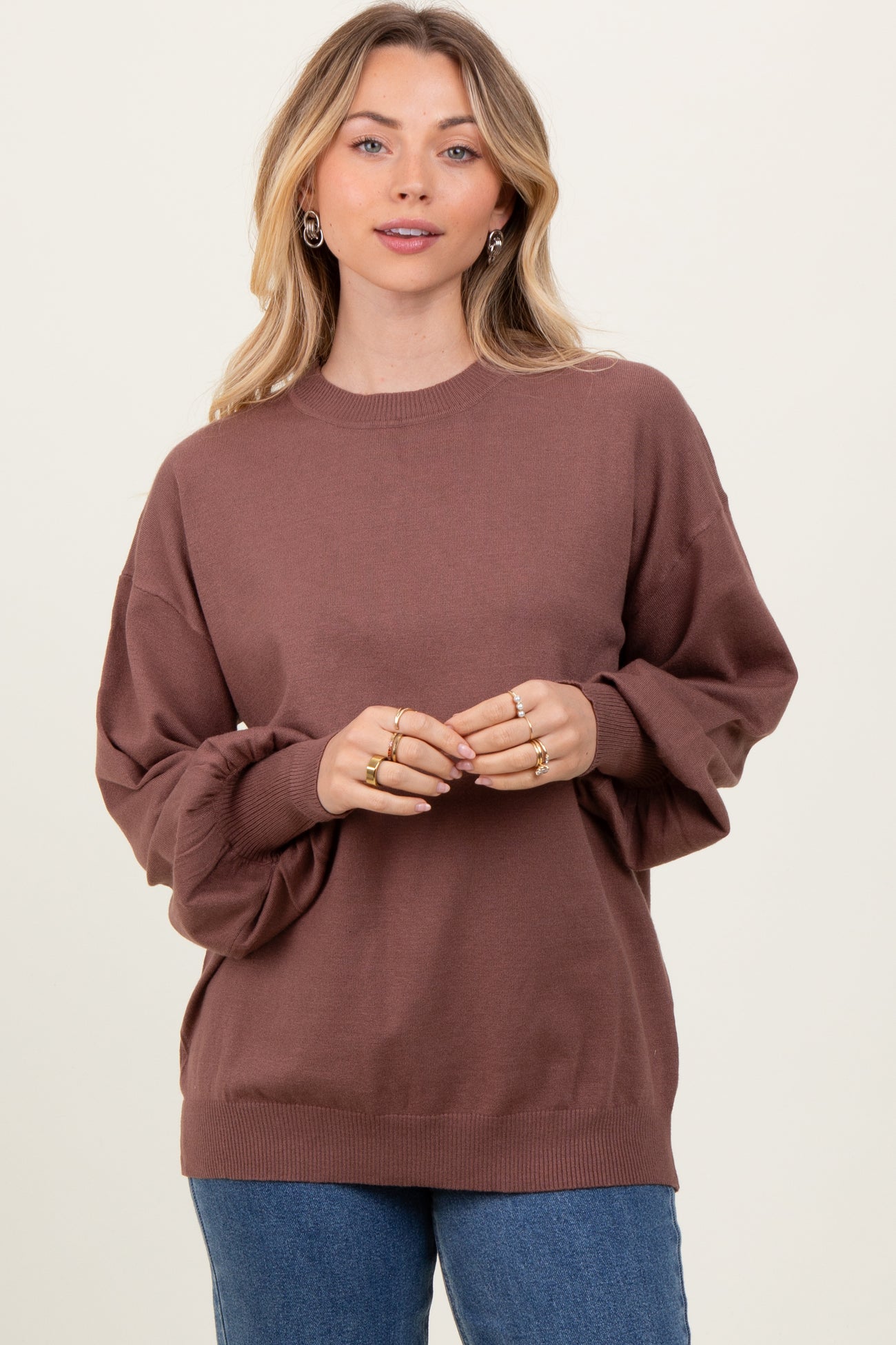 woman wearing a brown oversized sweater with puffed sleeves and a crew neckline, styled with light blue jeans