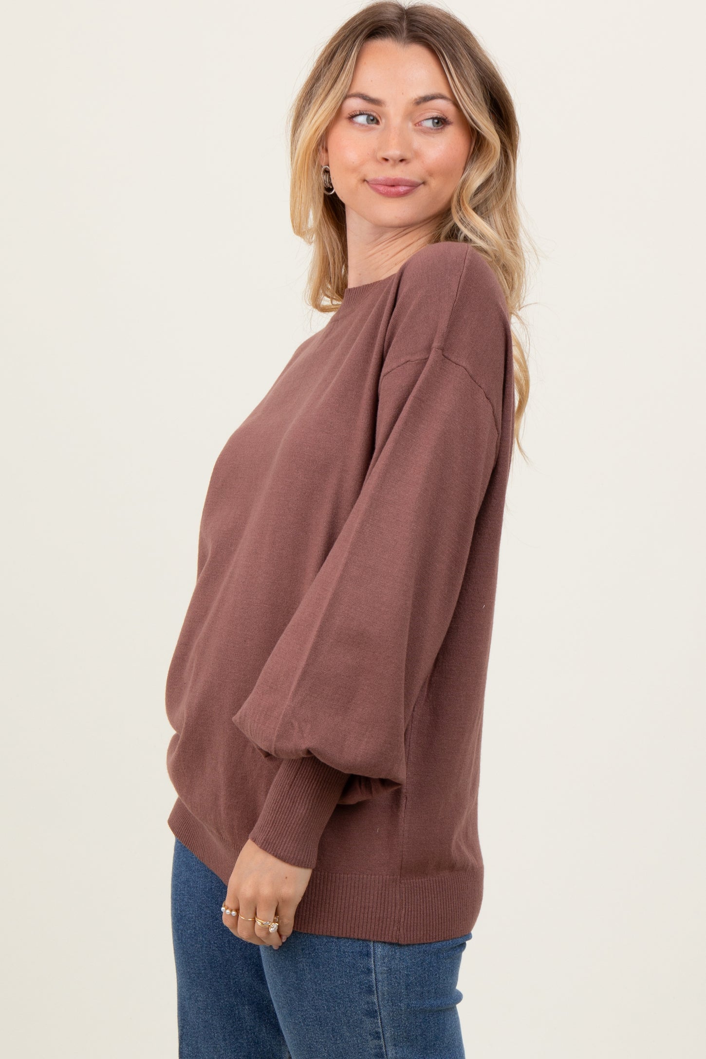 woman wearing a brown oversized sweater with puffy sleeves and a relaxed fit paired with blue jeans