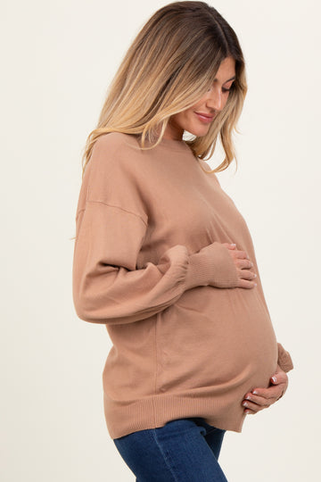 woman wearing a tan long sleeve maternity sweater and gently holding her baby bump