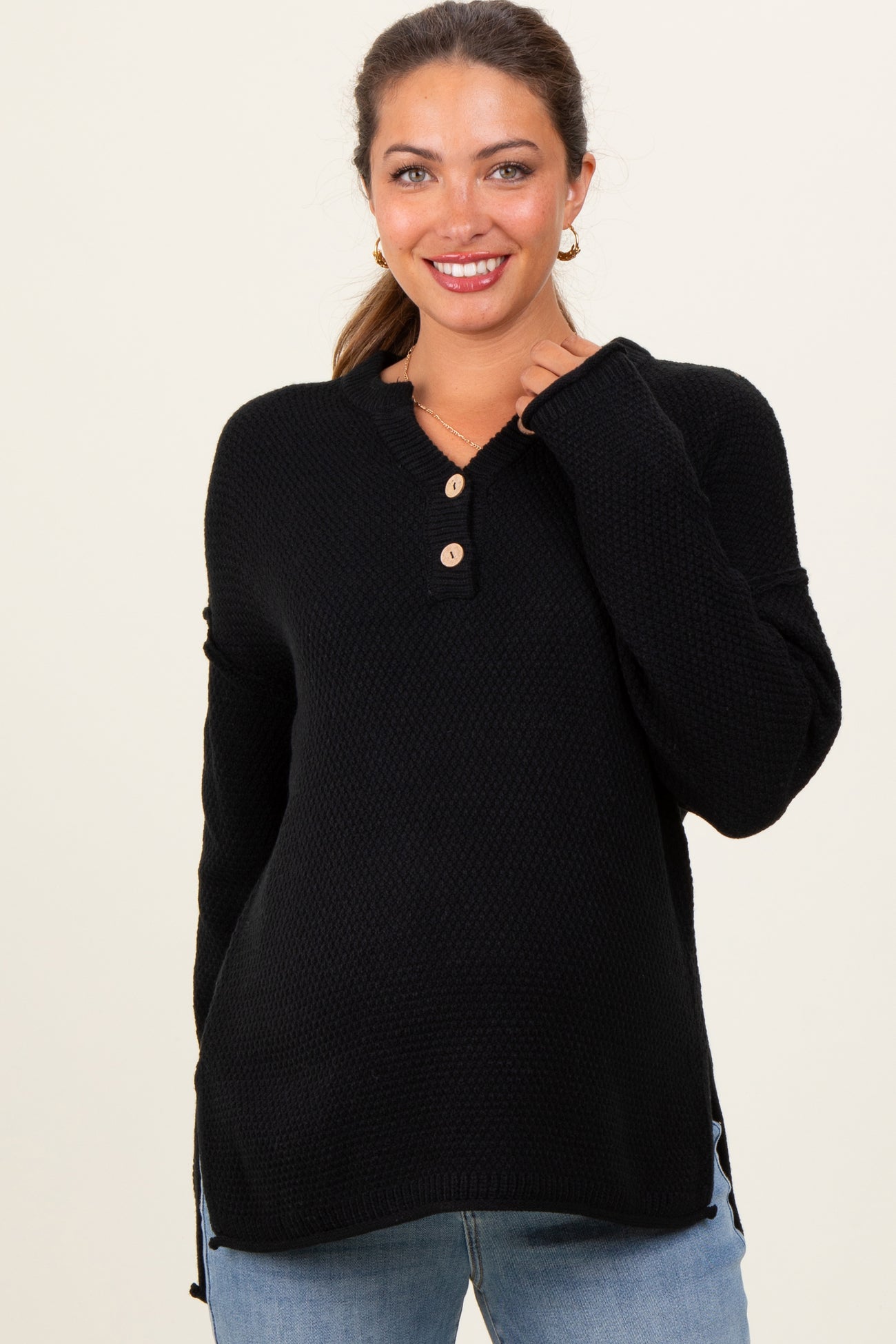 woman wearing a black maternity henley sweater with buttons and side slits, smiling at the camera