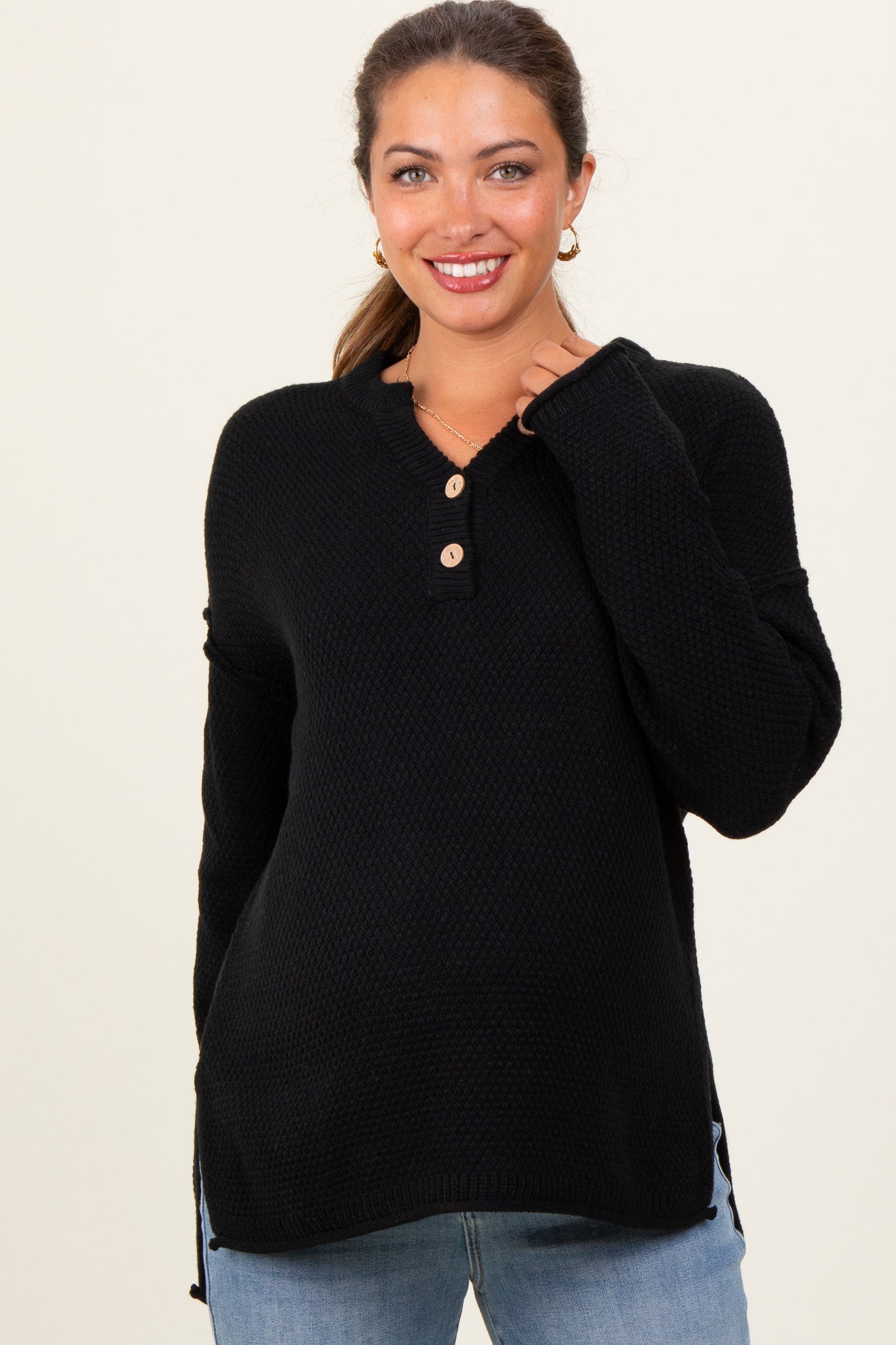 woman wearing a black maternity henley sweater with buttons and side slits, smiling at the camera