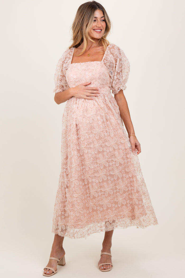 woman wearing a blush pink lace maternity dress with puff sleeves and a square neckline, holding her baby bump