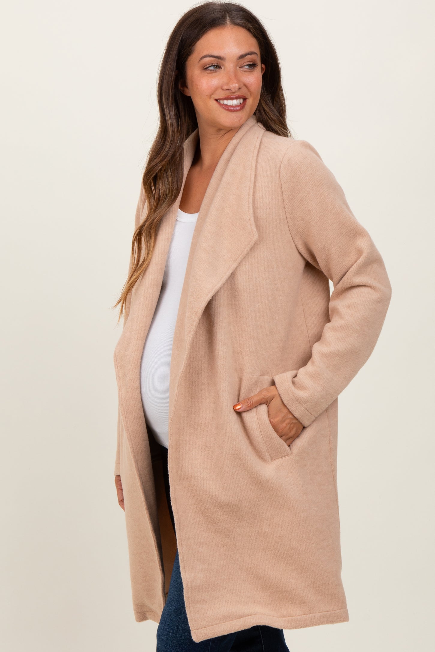 woman wearing a beige maternity wrap coat with pockets and a visible baby bump