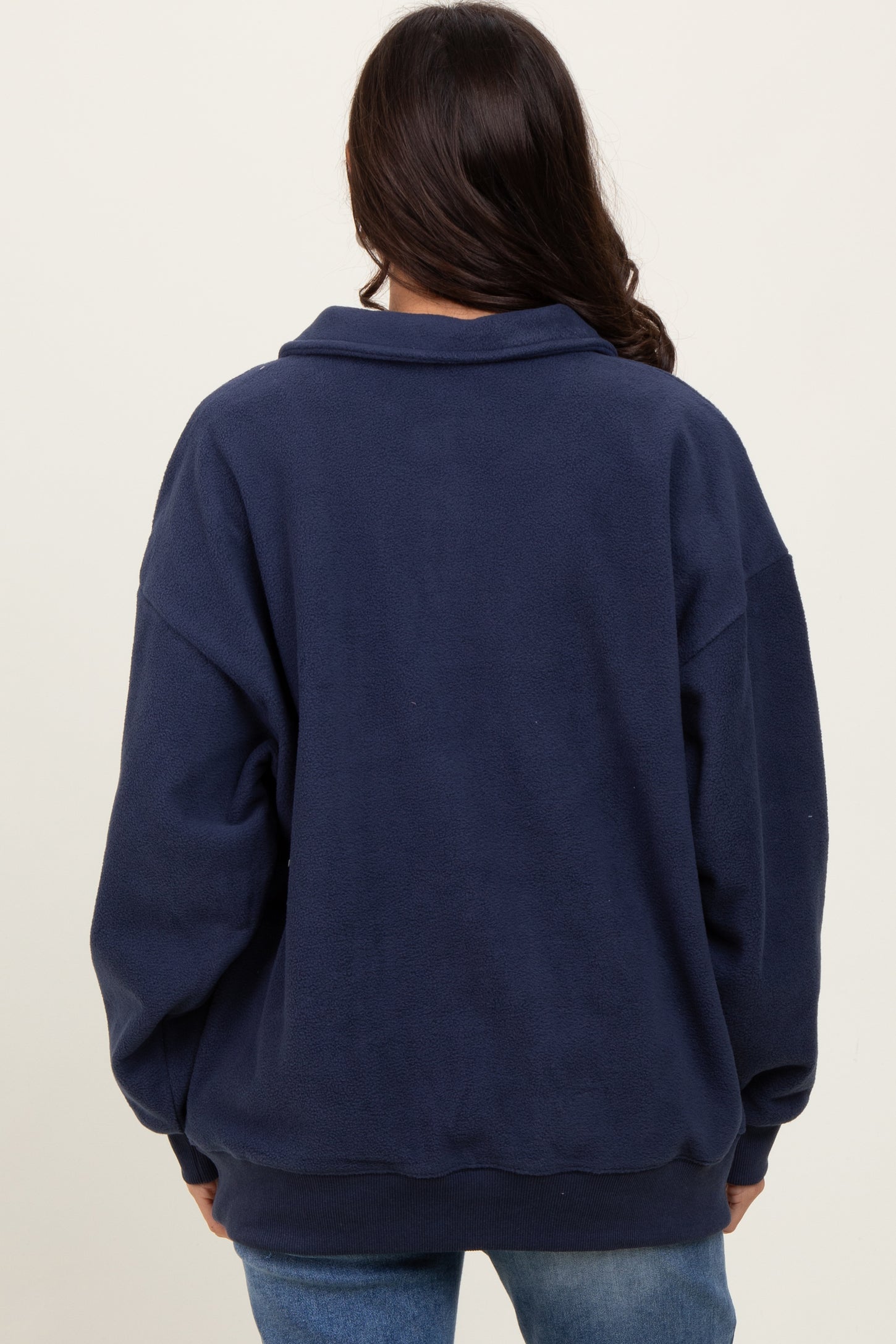 woman wearing a navy blue oversized fleece pullover with a collar and dropped shoulders, viewed from the back