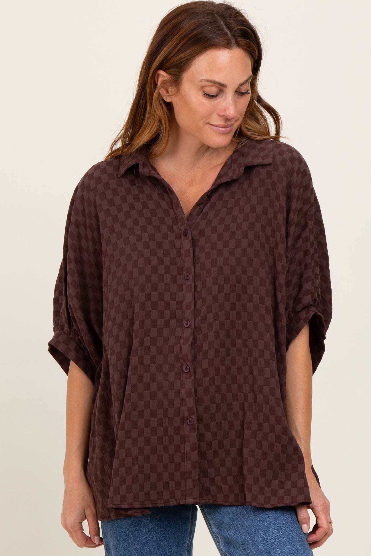 woman wearing a dark brown checkered oversized button-up shirt with rolled sleeves