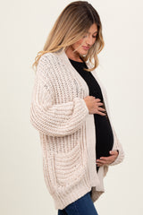woman wearing a cream chunky knit maternity cardigan and gently holding her baby bump