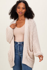 woman wearing a beige knitted cardigan with pockets over a light tank top and blue jeans