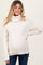 woman wearing a cream-colored maternity turtleneck sweater with a visible baby bump