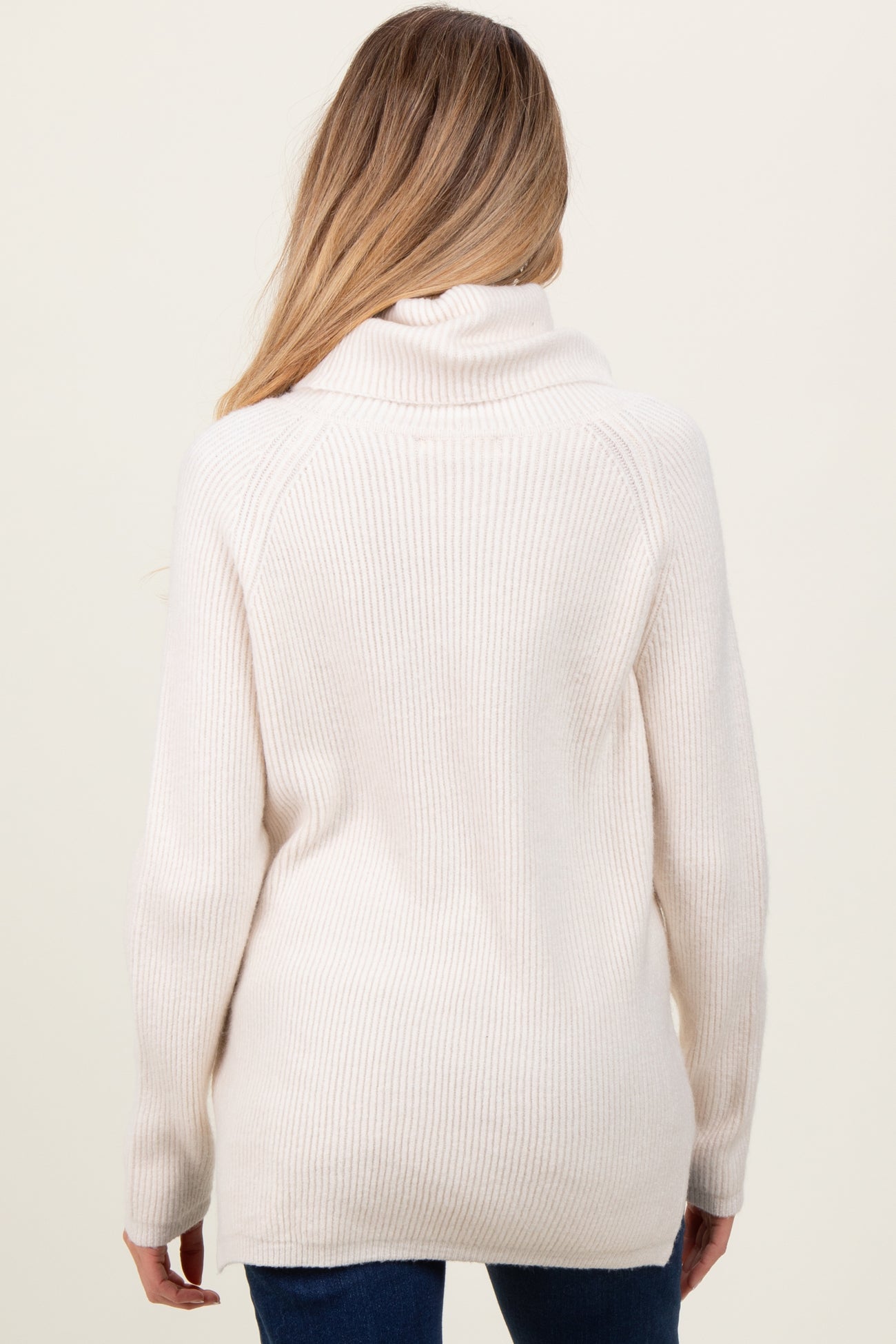 woman wearing a cream-colored maternity sweater with a cowl neck and ribbed texture, seen from the back