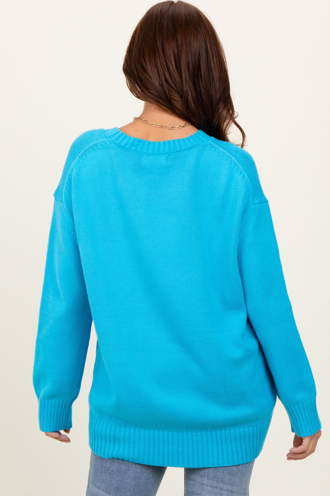 woman wearing a back view of a bright blue oversized sweater with ribbed cuffs and hem