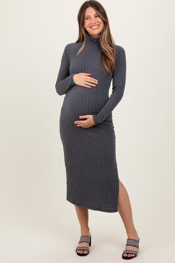 woman wearing a dark gray maternity dress with a turtleneck and side slit, holding her baby bump