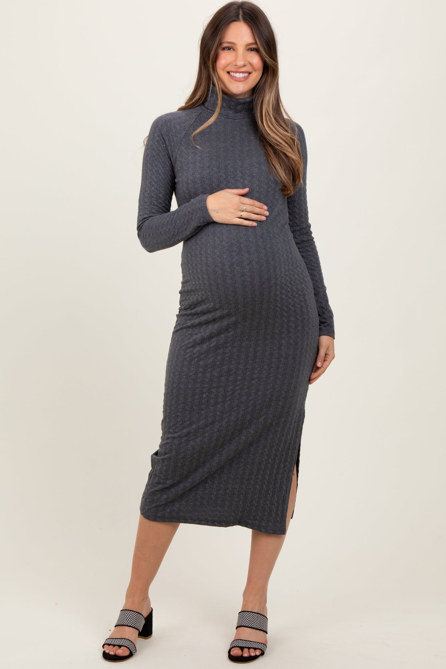 woman wearing a grey maternity dress with long sleeves and side slits, holding her baby bump