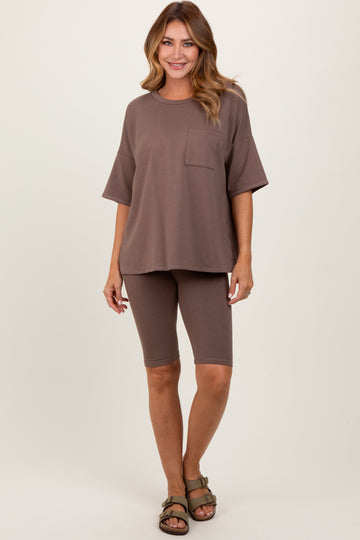 woman wearing a taupe oversized t-shirt with a pocket and matching bike shorts, standing against a neutral background