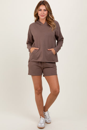 woman wearing a brown lightweight hoodie with pockets and matching brown shorts, standing on a neutral background