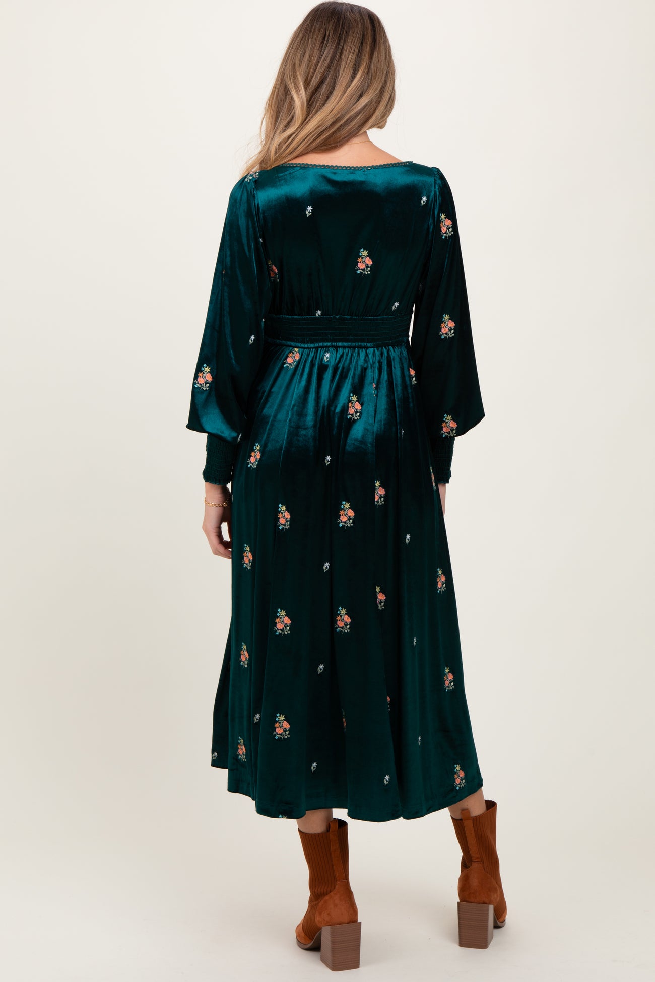 woman wearing a green velvet maternity dress with floral embroidery and long sleeves, standing with her back to the camera