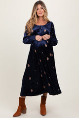 woman wearing a navy blue long sleeve maternity dress with floral embroidery and holding her baby bump