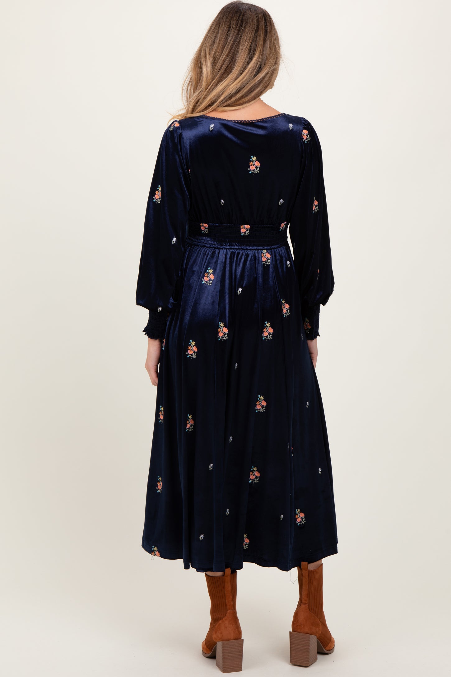 woman wearing a navy blue floral embroidered maternity dress with long sleeves and a flowing skirt