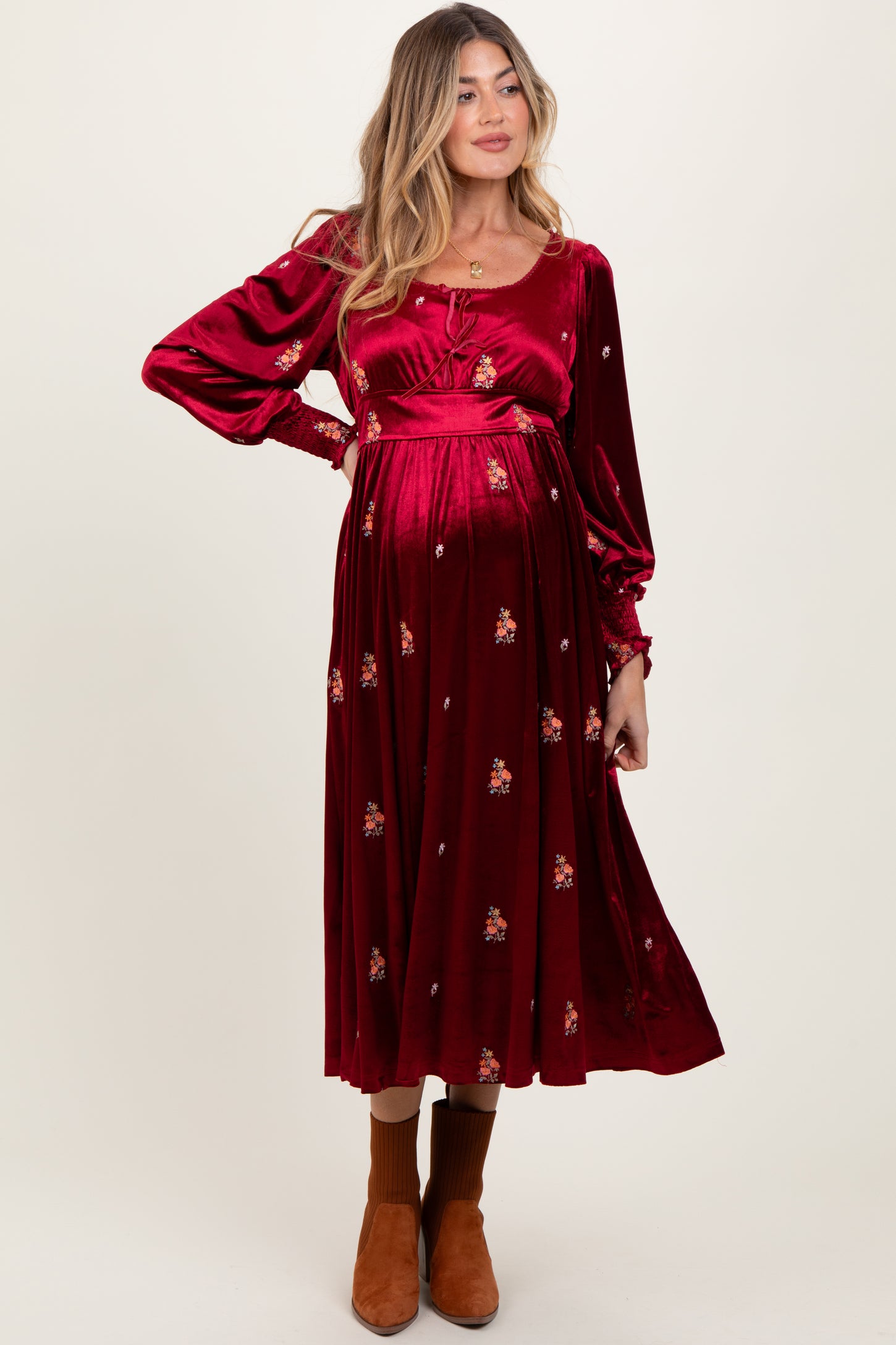woman wearing a burgundy maternity dress with long sleeves and floral embroidery, showing a baby bump