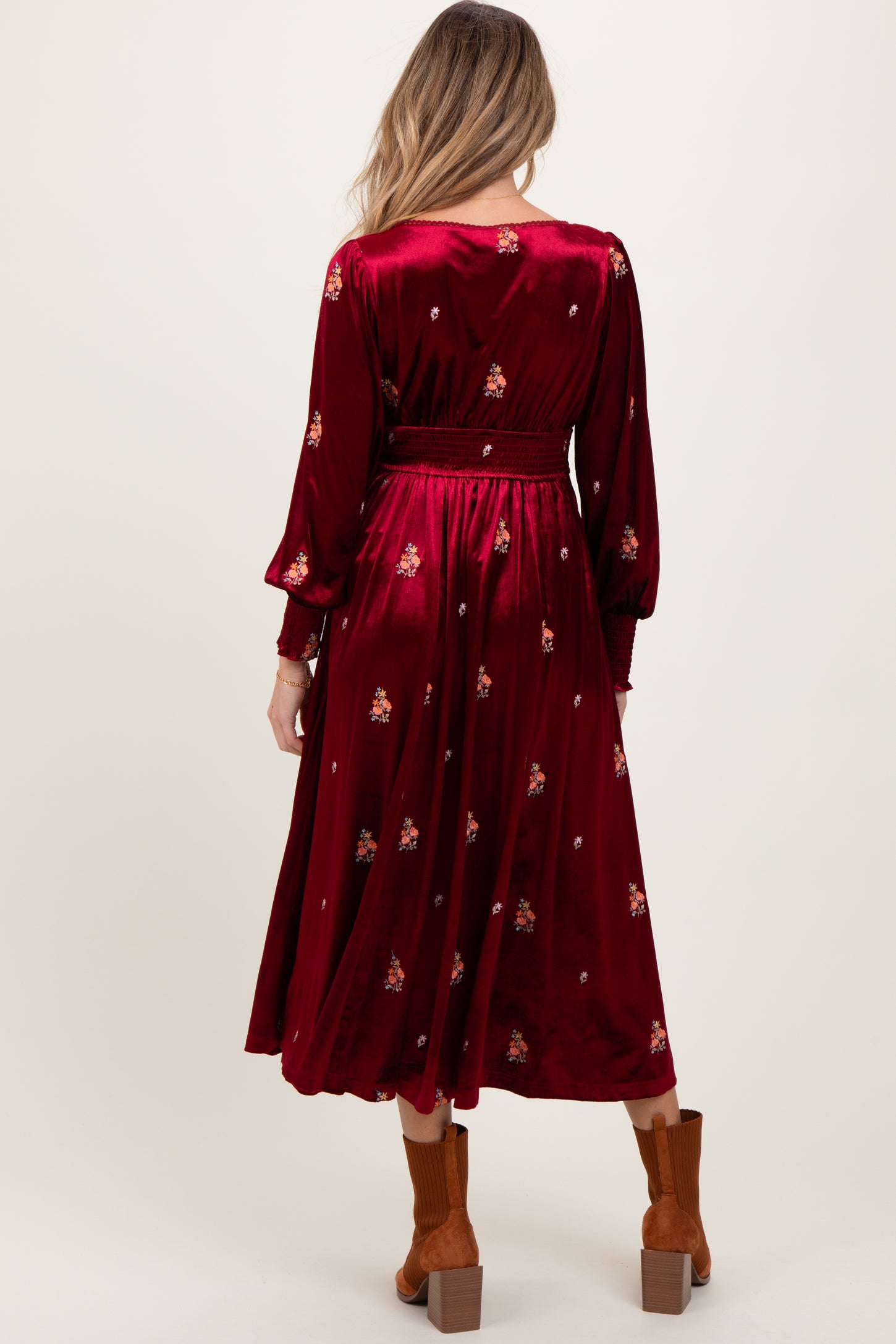 woman wearing a burgundy maternity dress with floral embellishments and long sleeves, showing her baby bump