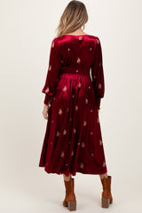 woman wearing a burgundy maternity dress with floral embellishments and long sleeves, showing her baby bump