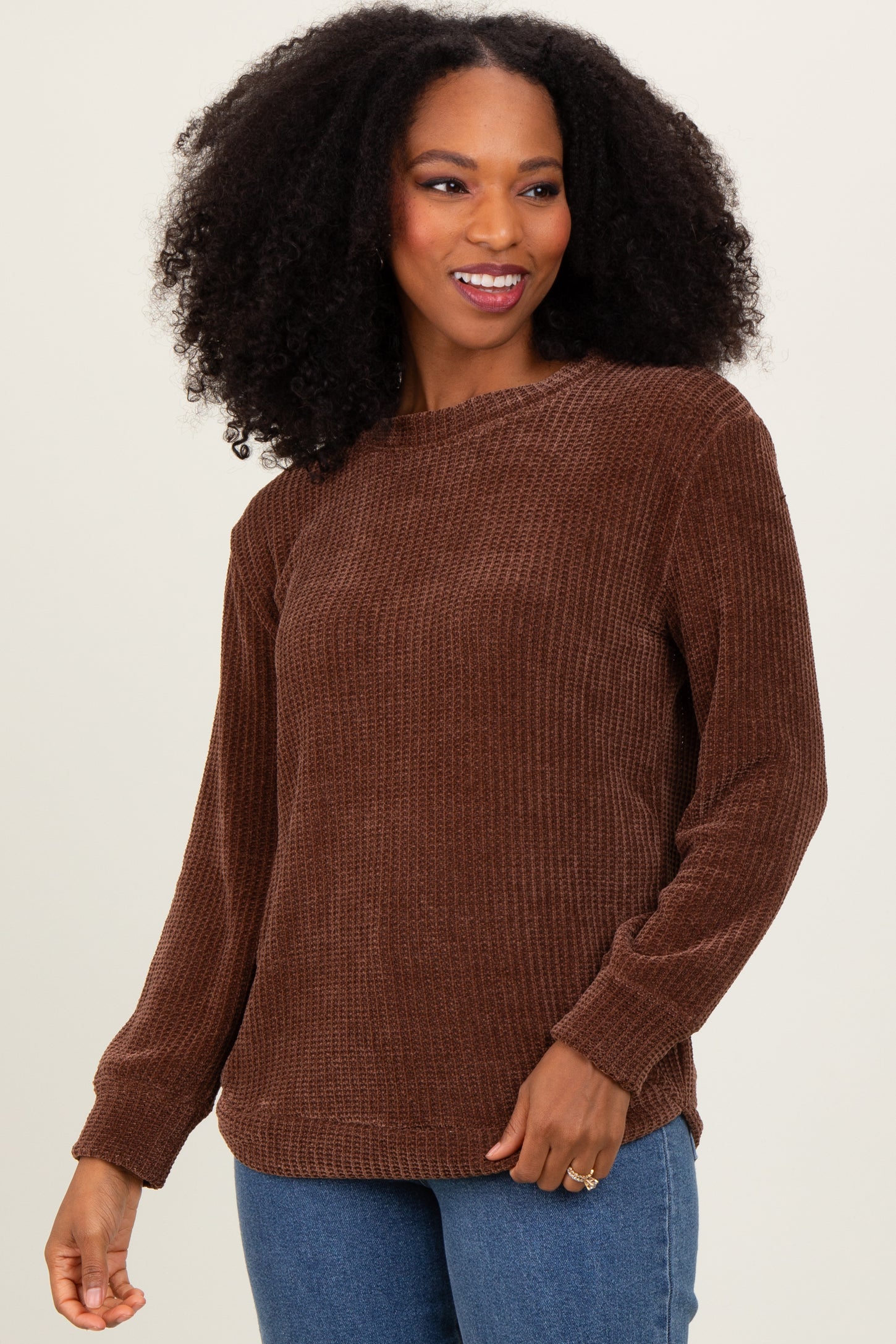 woman wearing a brown ribbed long sleeve sweater with a relaxed fit and side slits, smiling at the camera