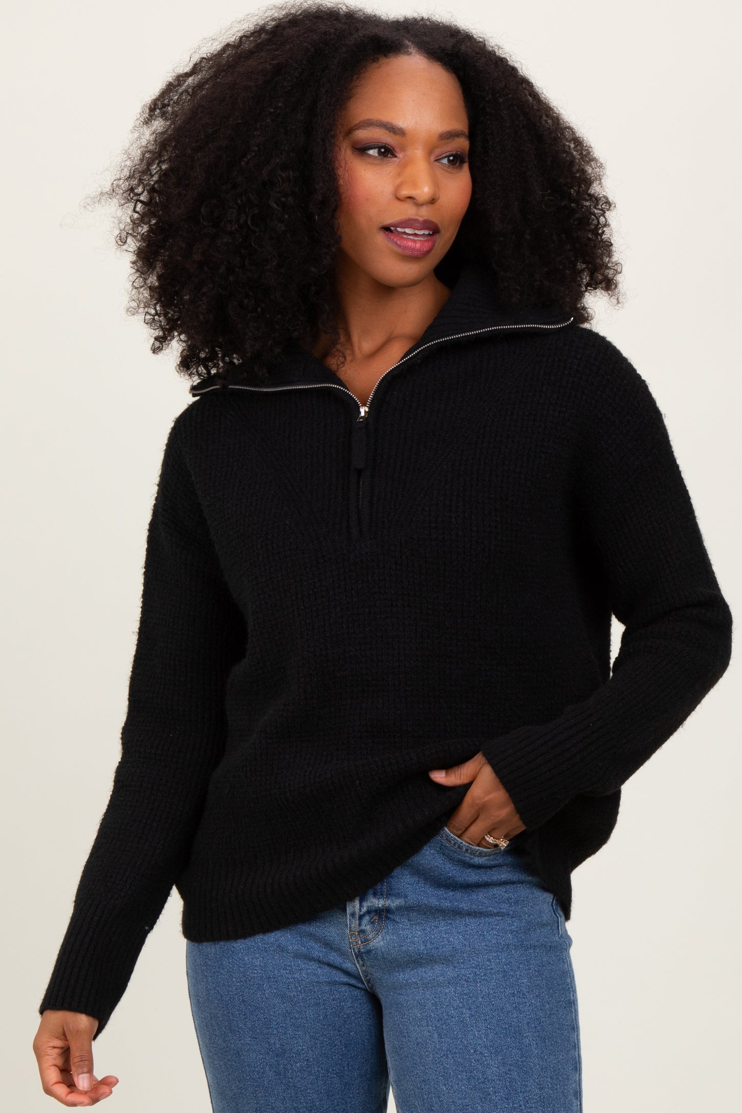 woman wearing a black zip-up sweater paired with blue jeans, showcasing a relaxed style and textured fabric