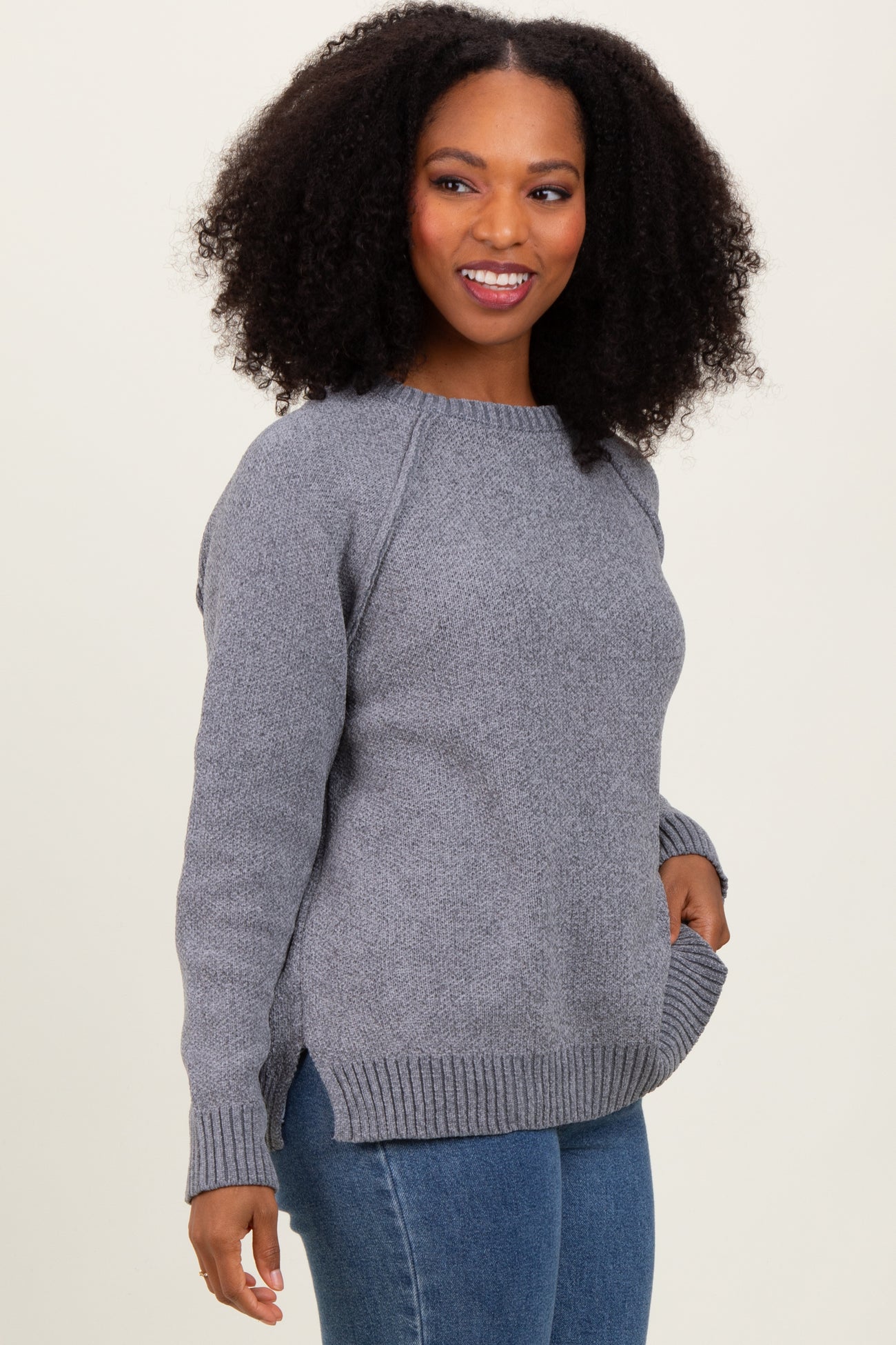 woman wearing a gray knit sweater with side slits and raglan sleeves, paired with blue jeans