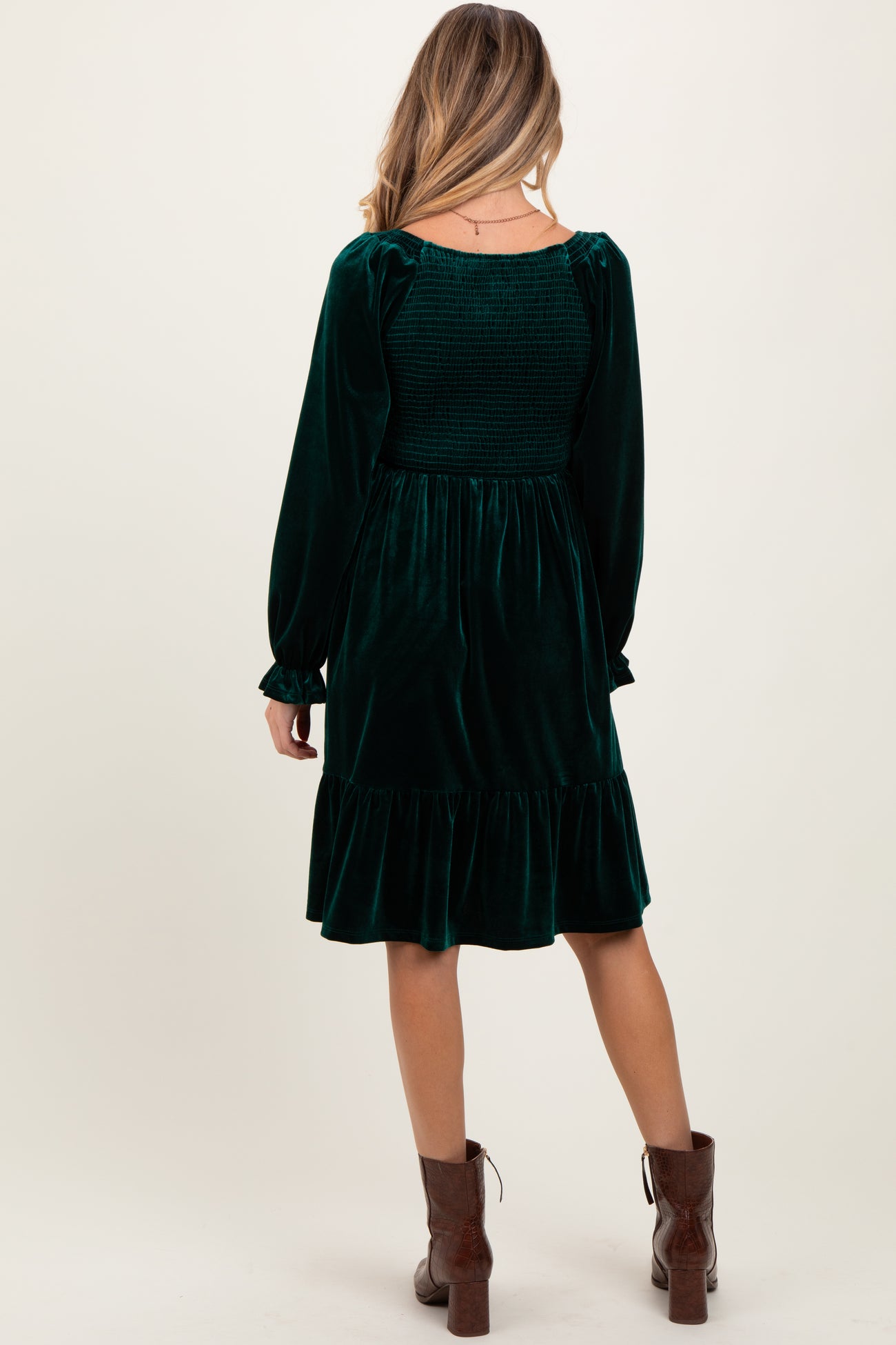 woman wearing a dark green velvet maternity dress with long sleeves and a ruffled hem