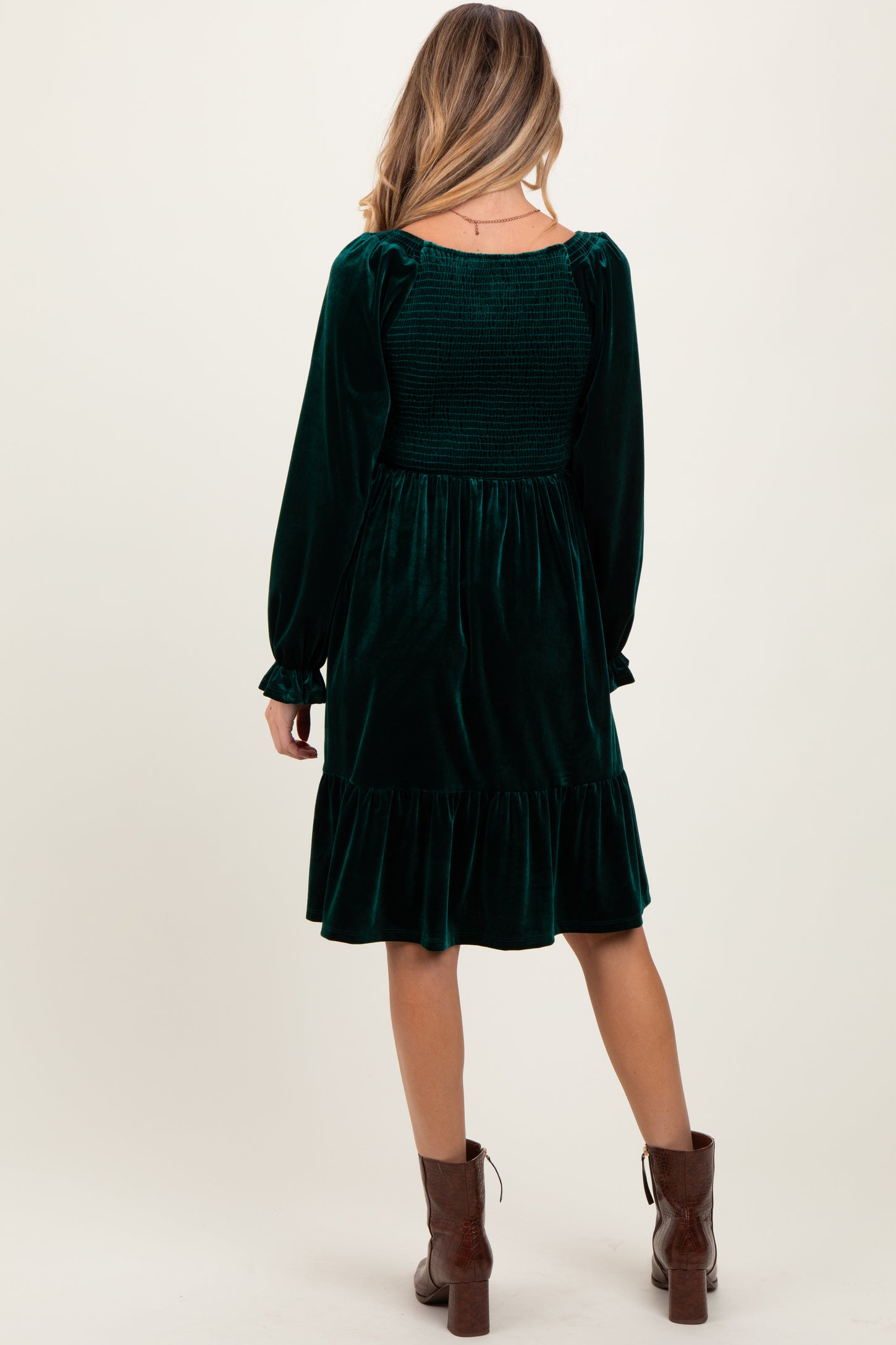 woman wearing a dark green velvet maternity dress with long sleeves and a ruffled hem